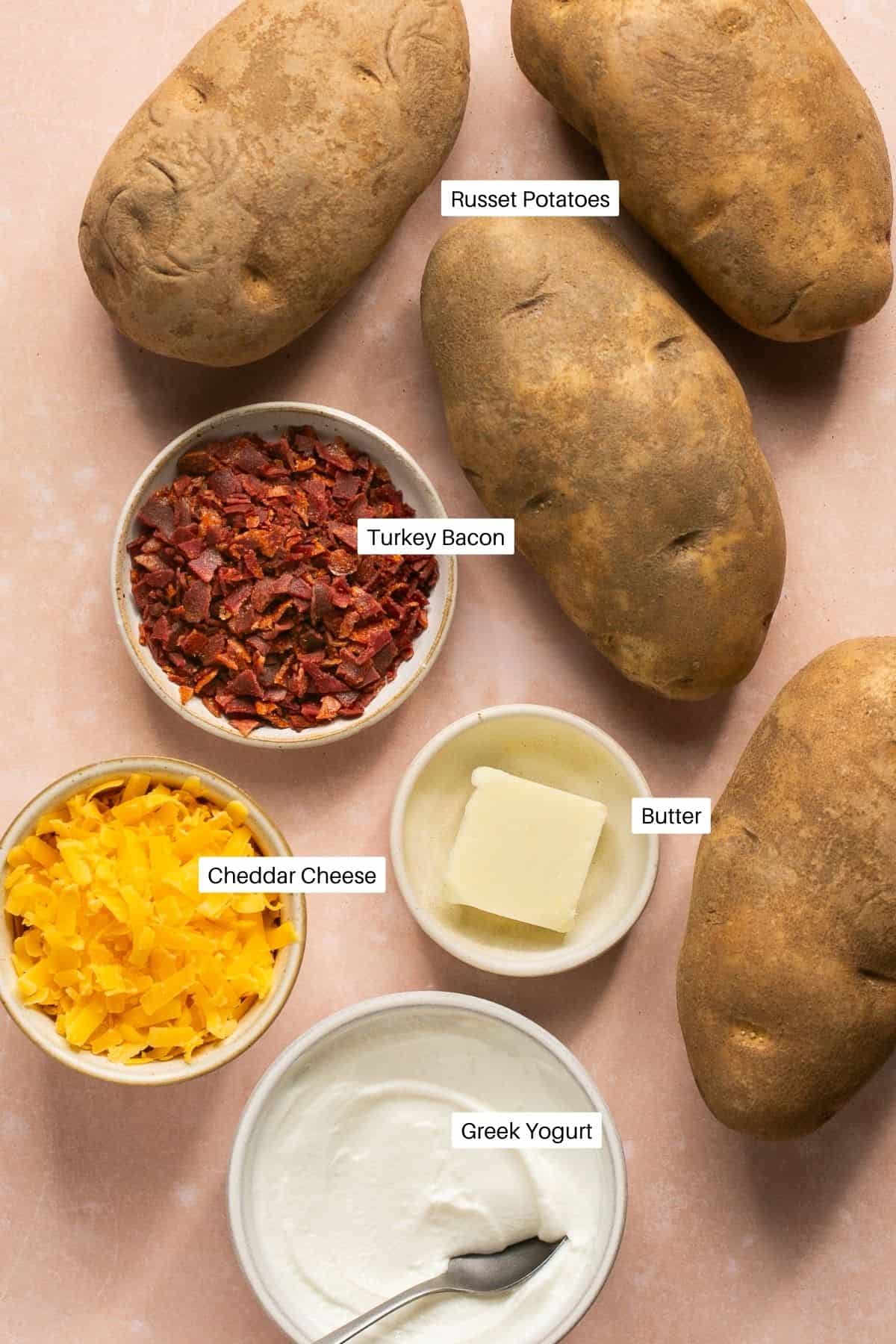 Russet potatoes, cooked turkey bacon, shredded cheese, butter and greek yogurt laid out for baked potatoes.