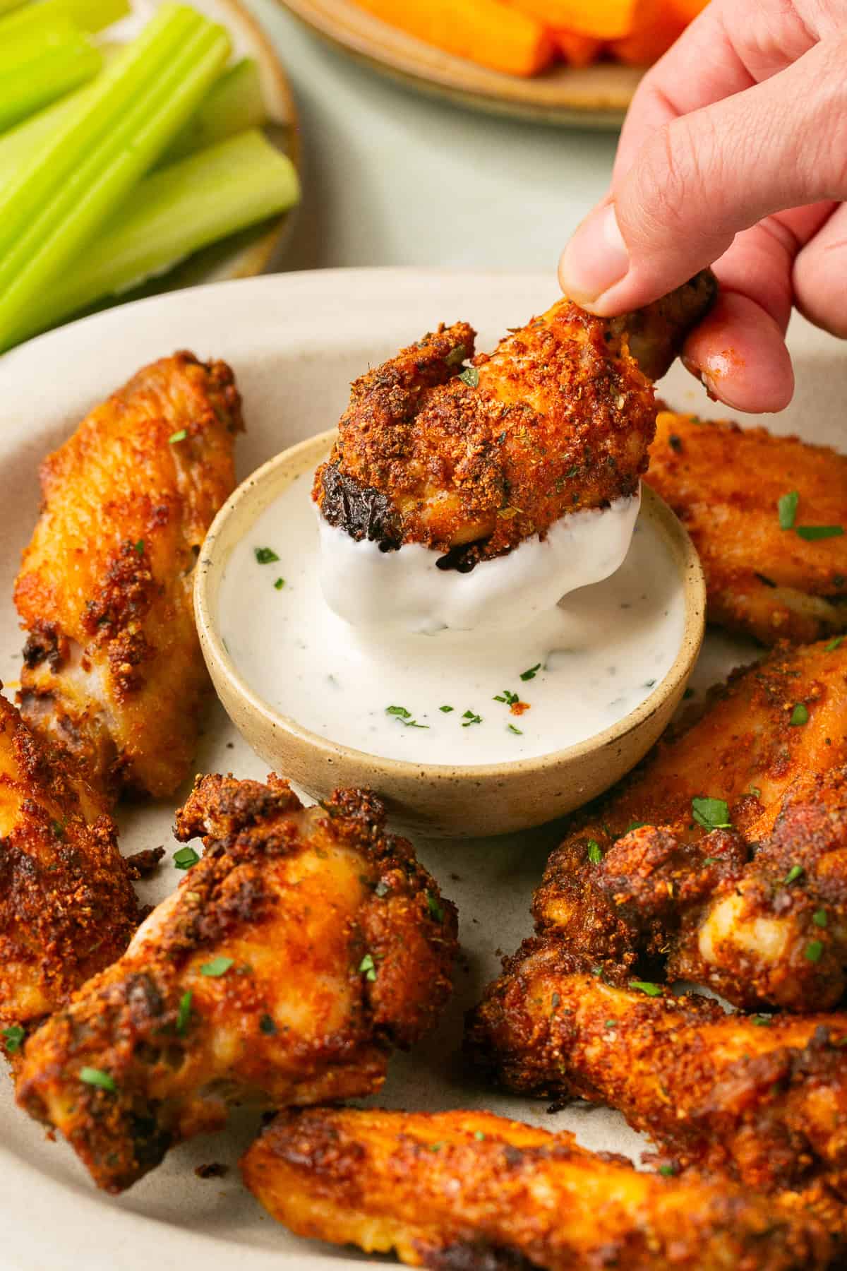 Crispy dry rub wings on a serving plate with a person holding one and dipping it into ranch dressing. 
