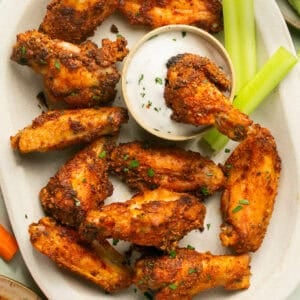 Wings on a servings platter with ranch in the center in a small bowl and celery sticks.