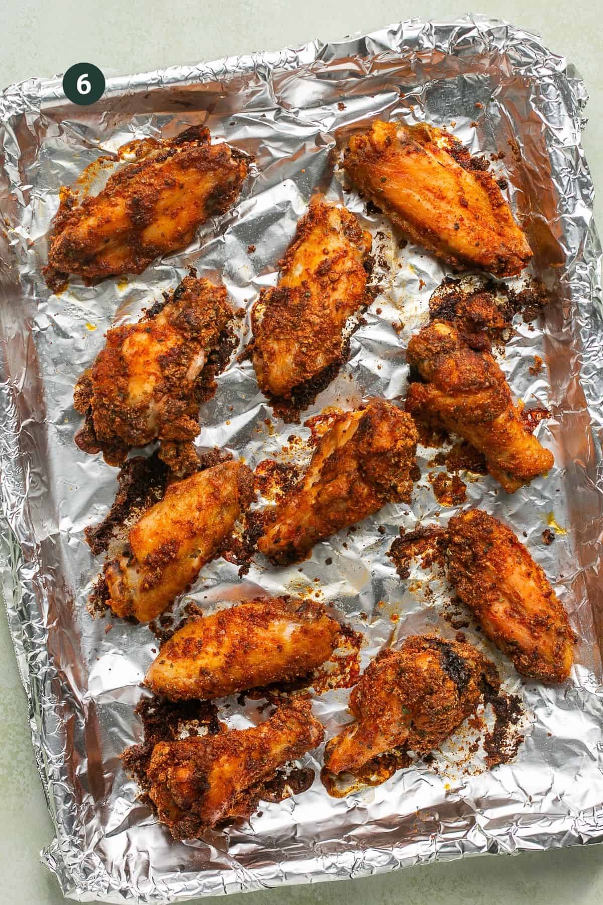 Freshly baked crispy seasoned wings on a foil lined baking sheet.