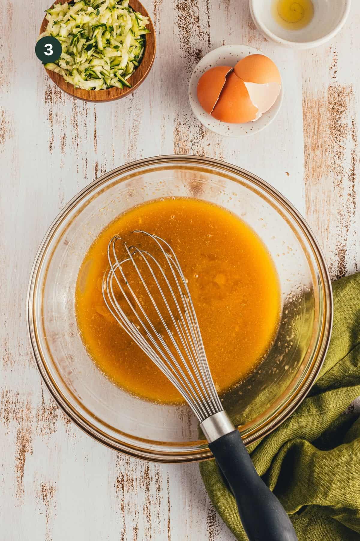 Honey, applesauce, olive oil, vanilla extract and eggs mixing in a bowl with a whisk.