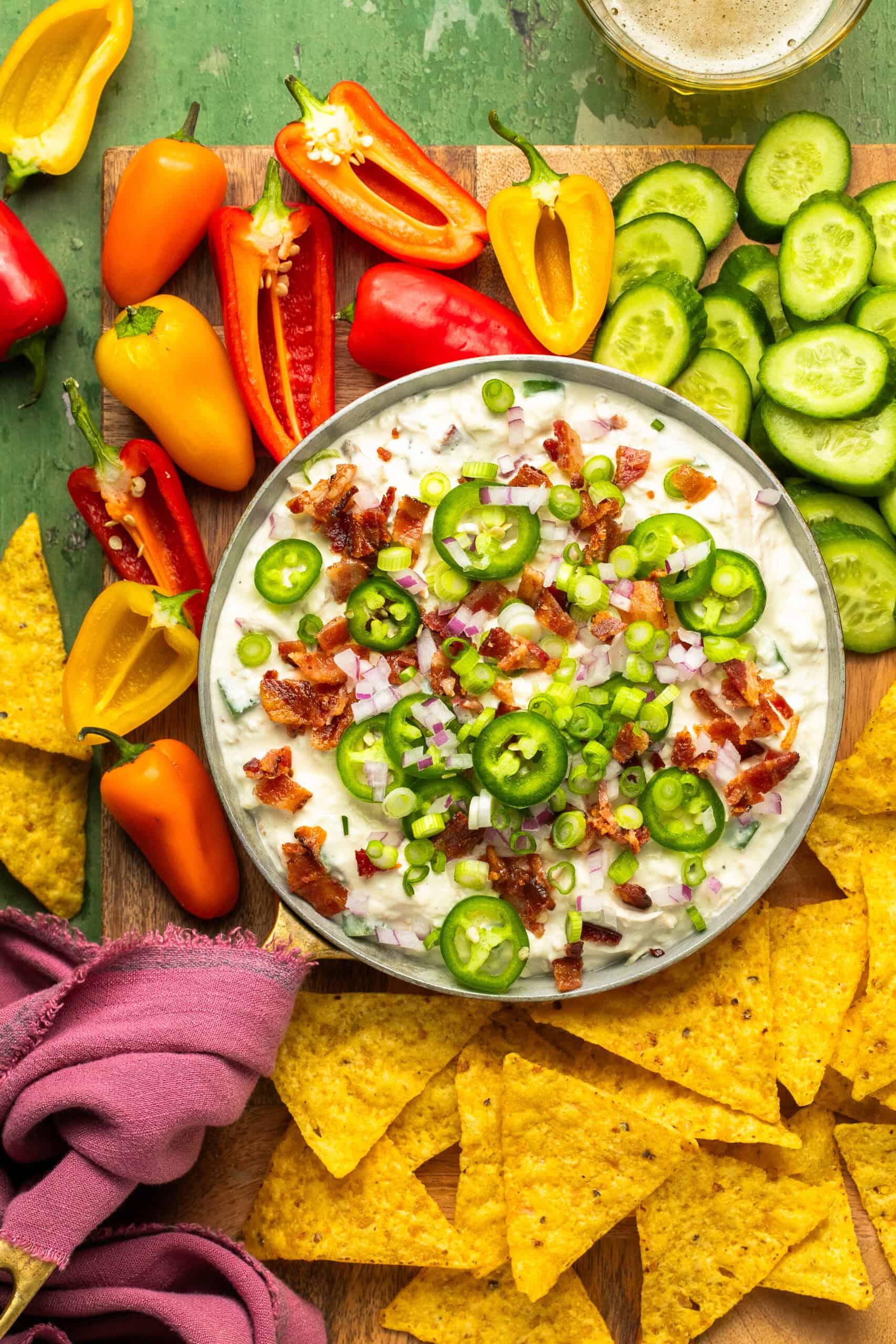 Jalapeno popper dip in a serving bowl surrounded by chopped veggies and chips for dipping.