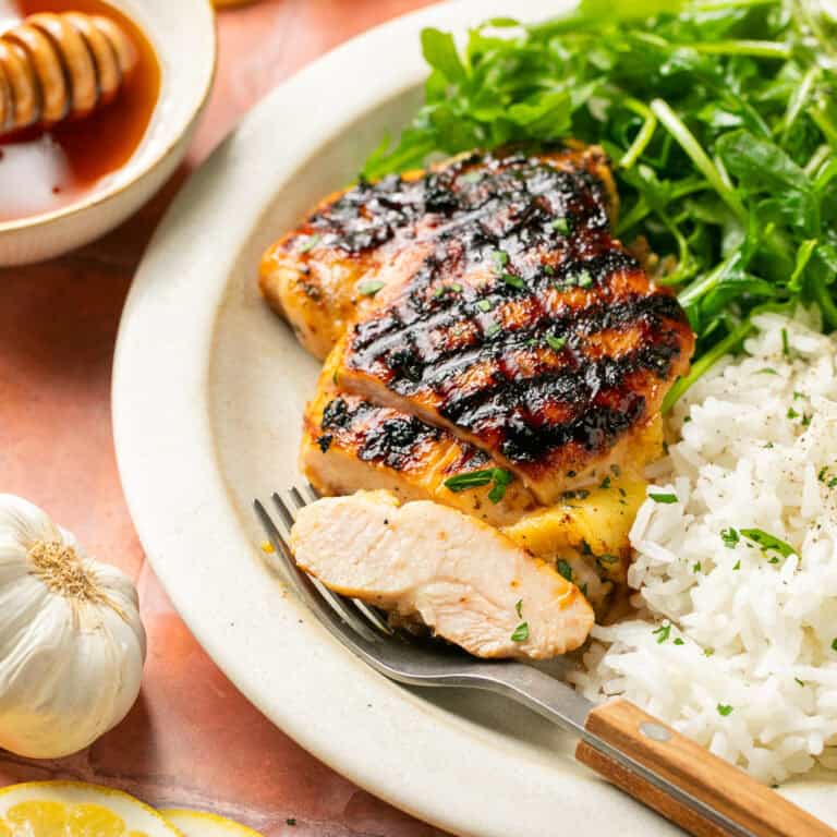 Marinated chicken thighs with a slice cut on a plate with arugula salad and white rice.