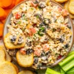 Cottage cheese dip loaded with olives, bell peppers, cheese and taco seasoning with crunchy crackers dipped in it in a bowl.