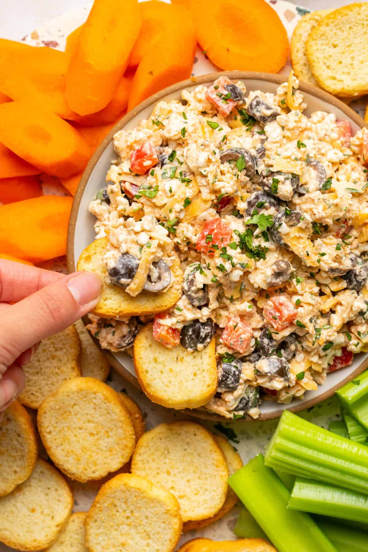 Cottage cheese queso dip in a serving bowl with hands dipping crispy bread crackers in to the bowl with veggies around the outside. 