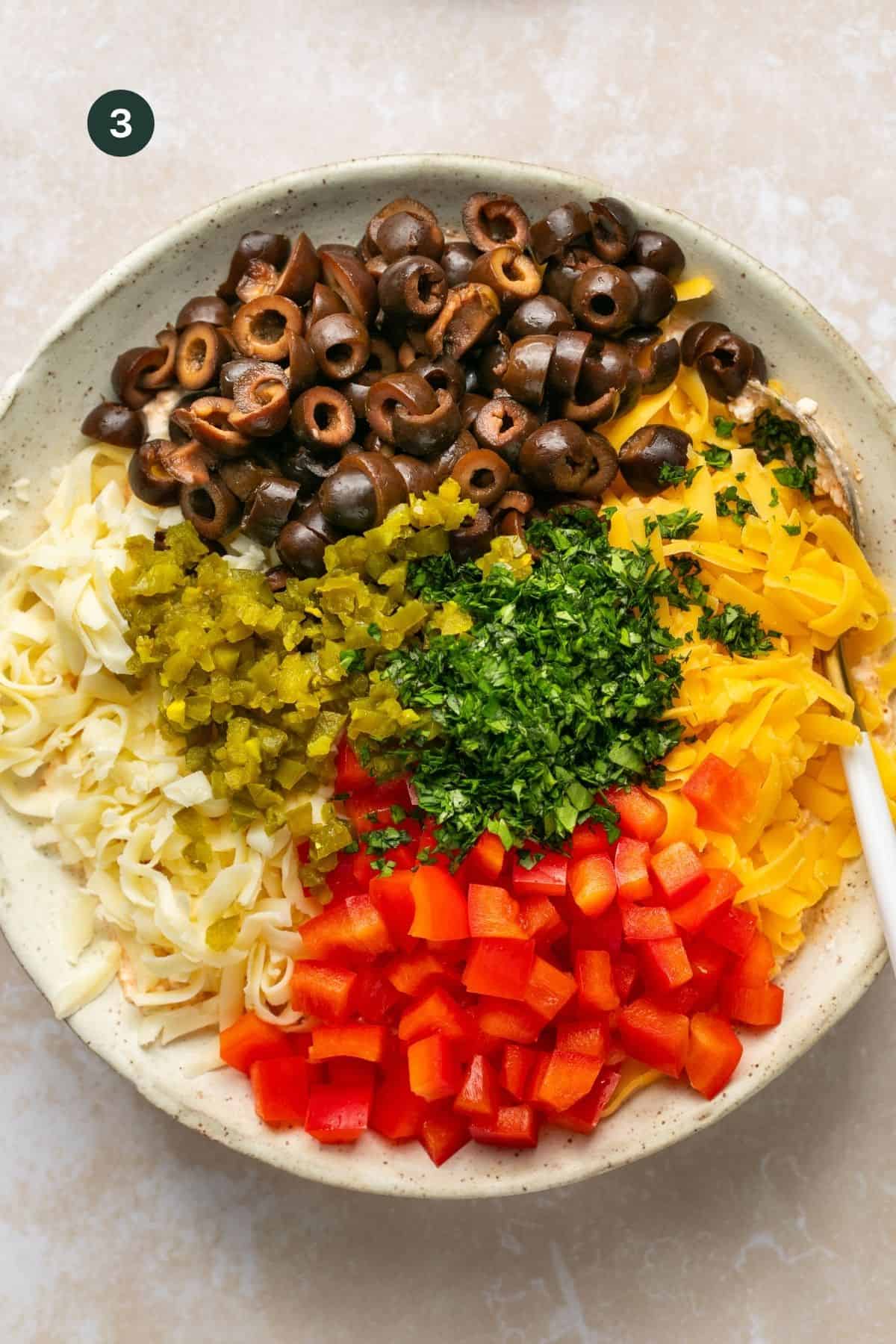 Olives, jalapenos, cheddar cheese, pepper jack cheese, bell peppers and cilantro added to the bowl with the cream cheese to combine. 