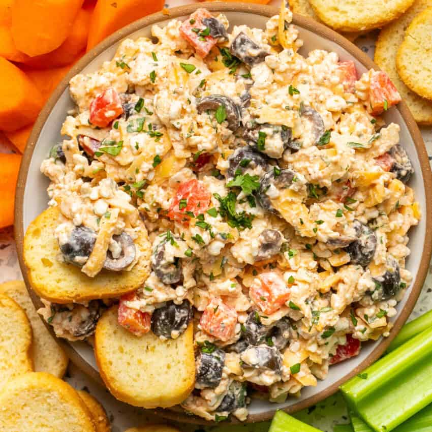 Cottage cheese dip loaded with olives, bell peppers, cheese and taco seasoning with crunchy crackers dipped in it in a bowl.