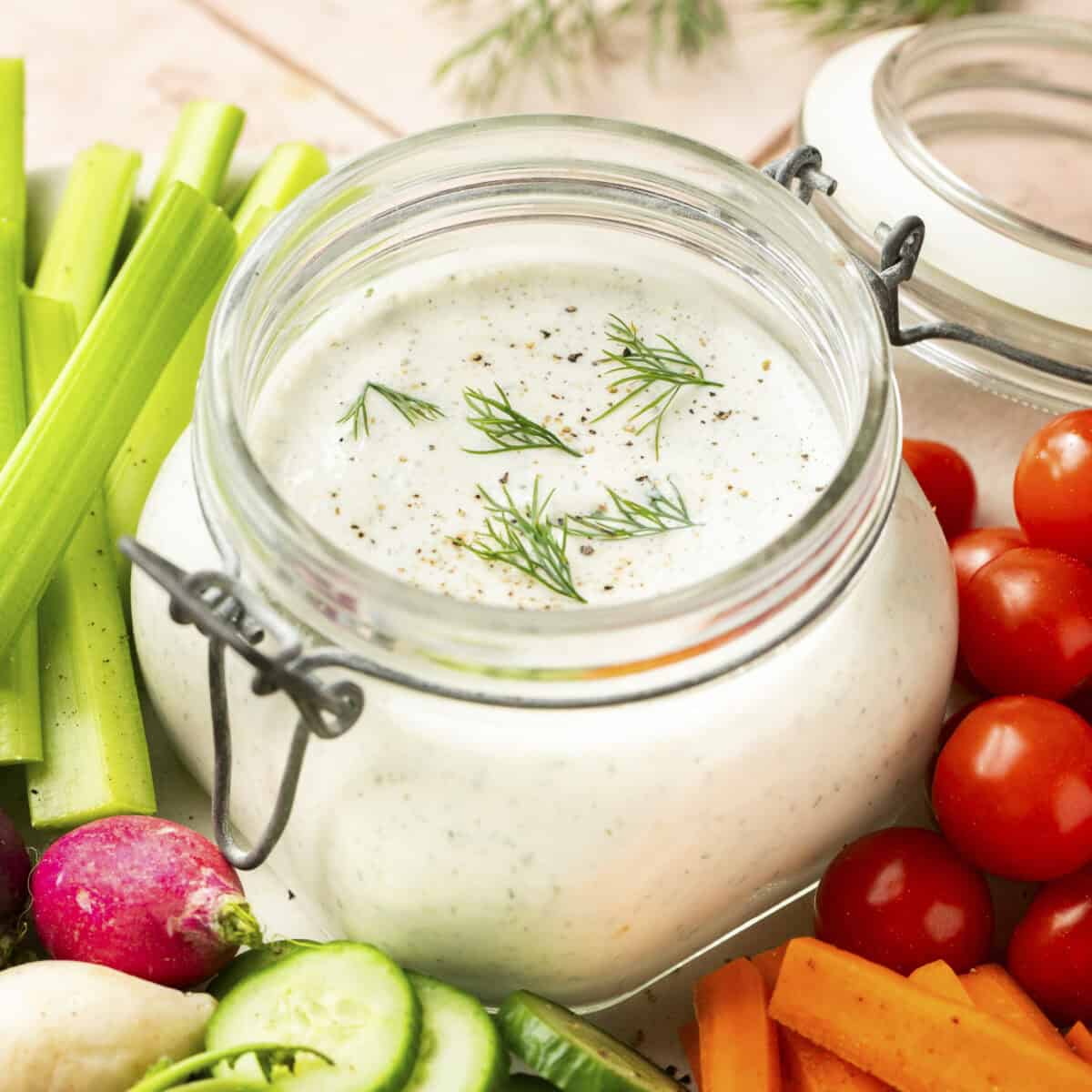 Cottage cheese based ranch dip in a sealable container with veggies around it.