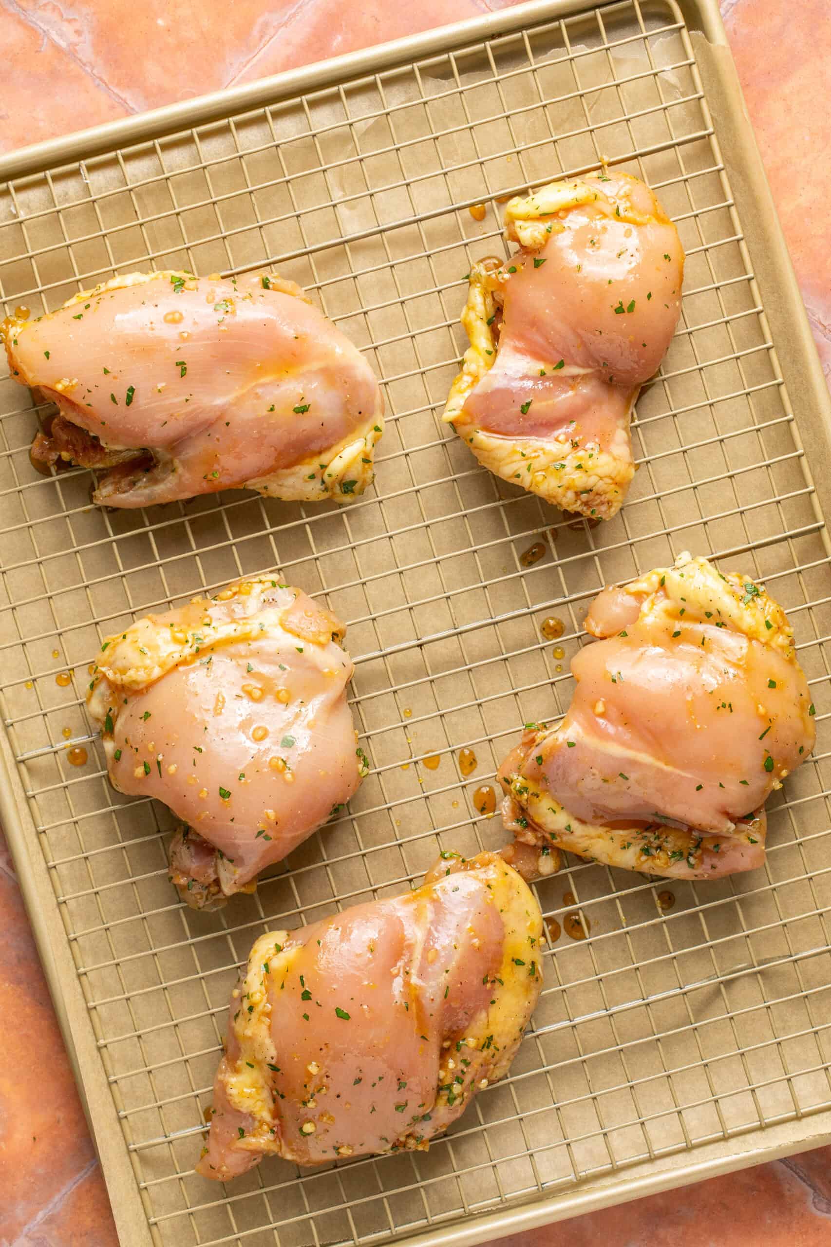 Chicken thighs on a baking sheet with a cooling rack to lift off the pan when cooking in the oven to get crispy.