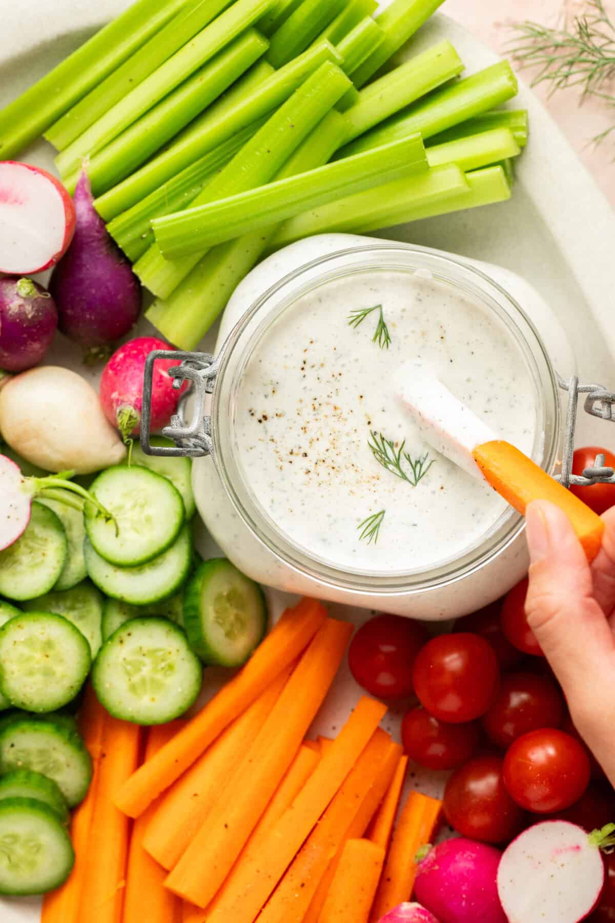 Carrot dipping into ranch dip with other veggies around on a platter. 