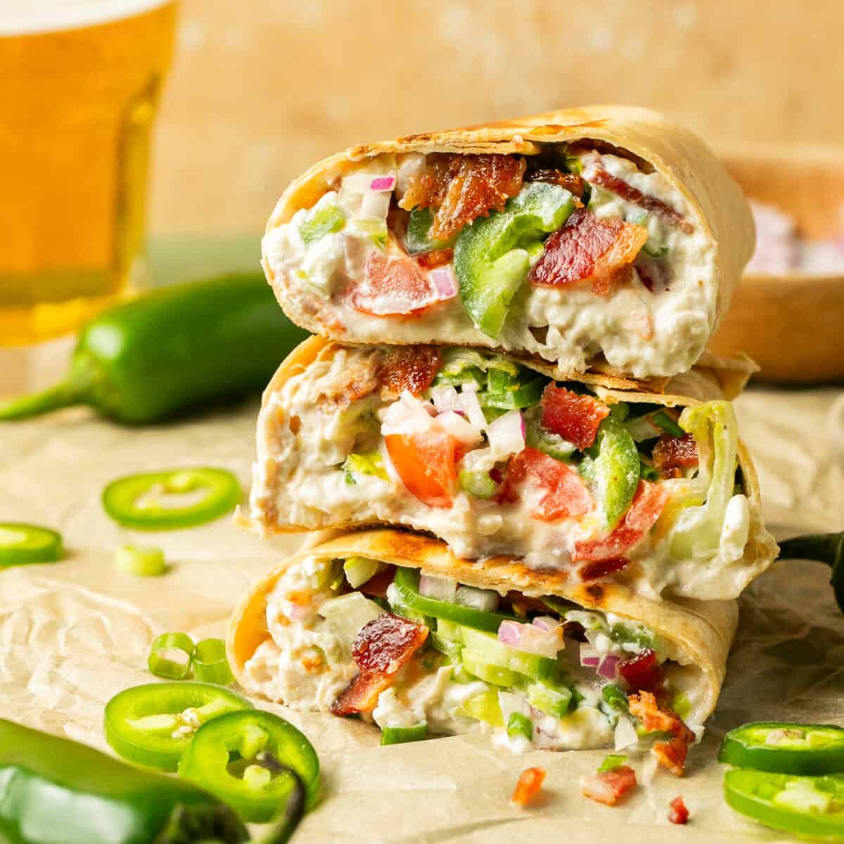 Three stacked jalapeno popper shredded chicken wraps with the inside showing.