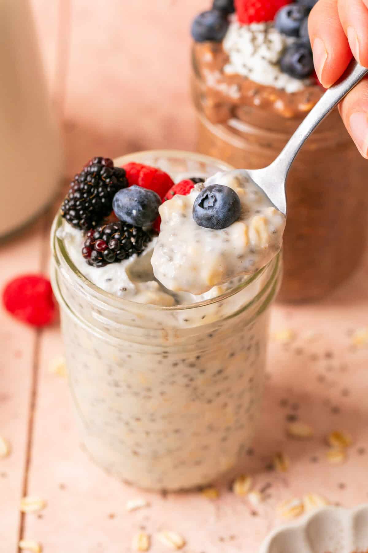 Vanilla chia overnight oats with mixed berries on top and a hand holding a spoon with some on it. 