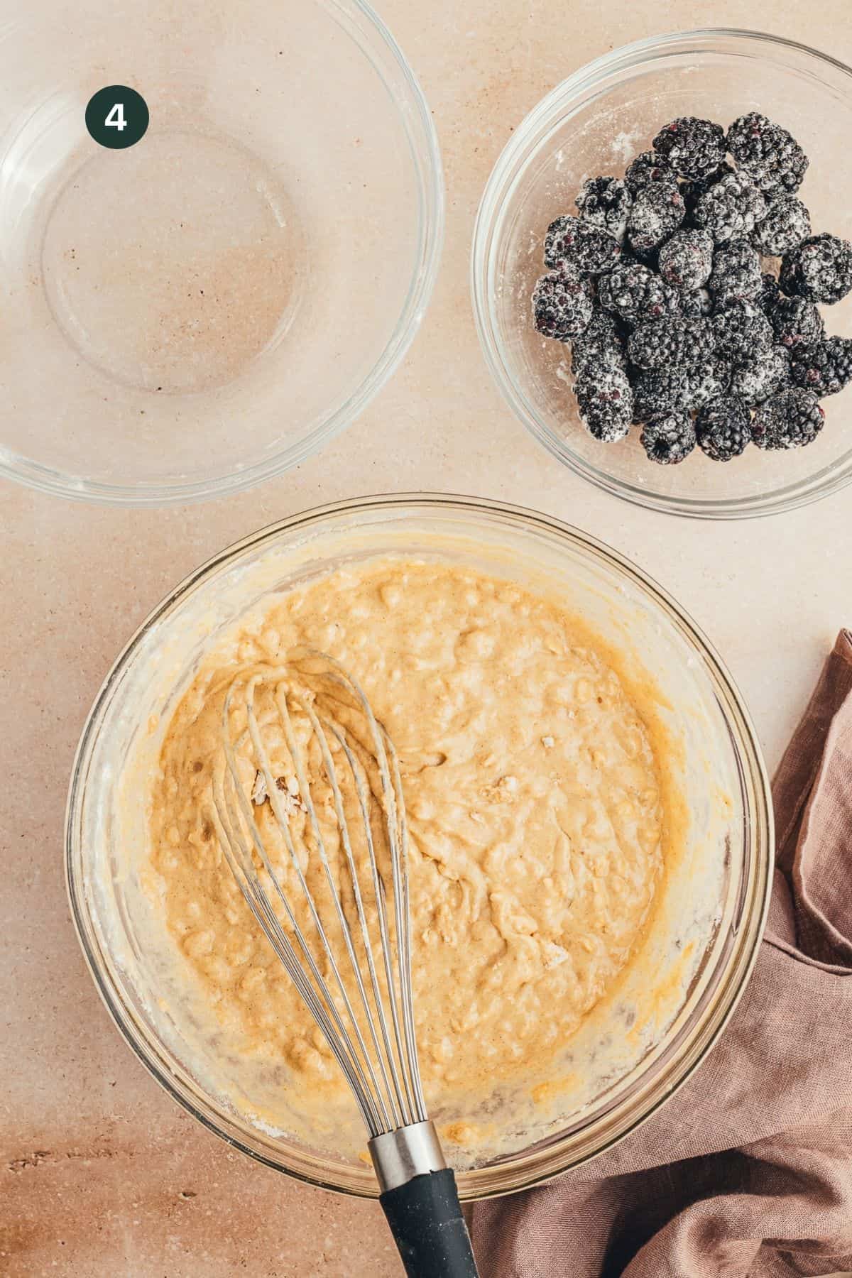 Wet and dry muffin ingredients combined in a mixing bowl with blackberries on the side.