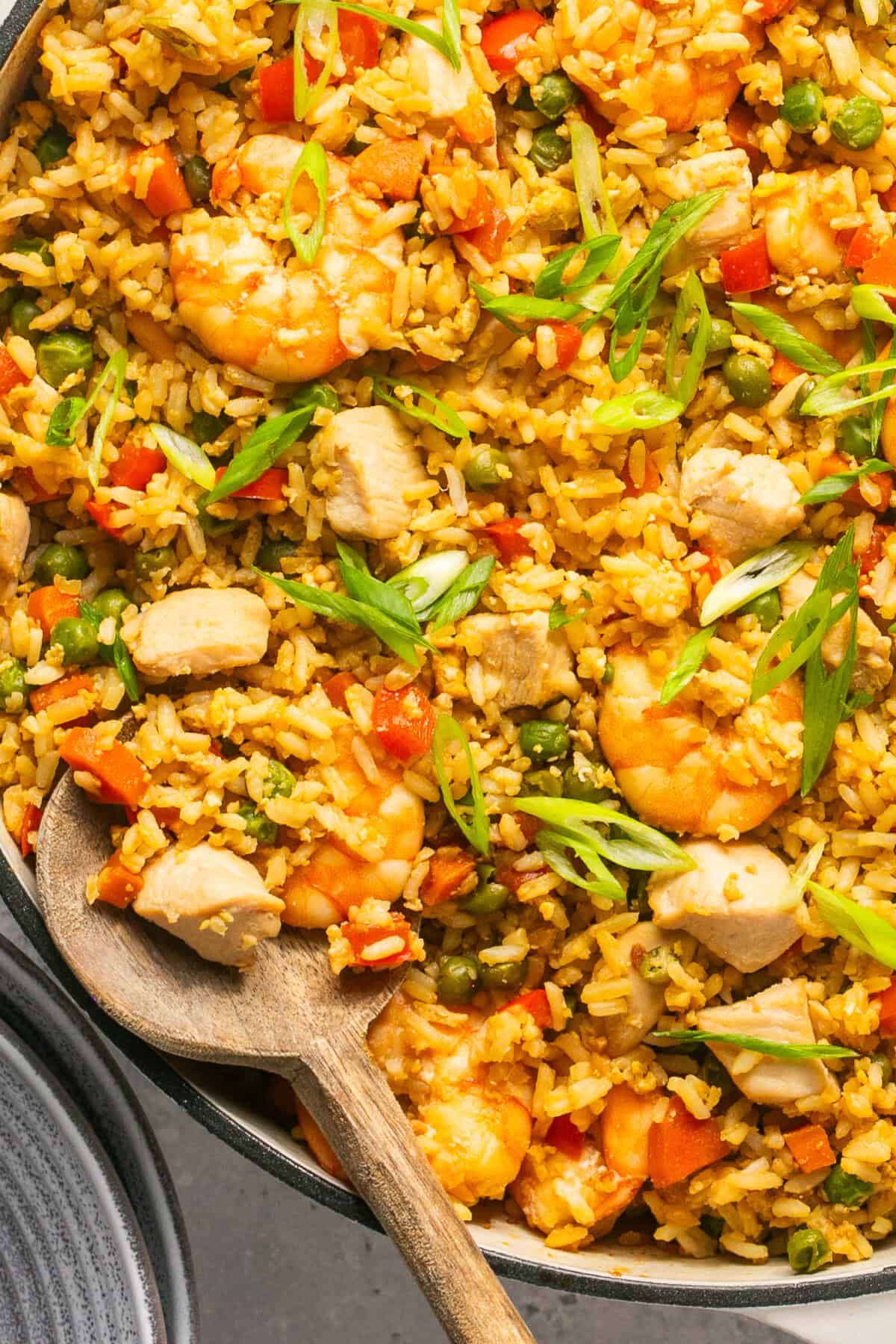 Close up image of chicken and shrimp fried rice with a wooden spoon and green onions on top.