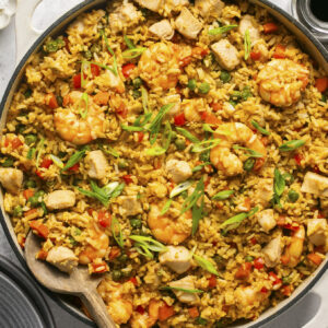 Chicken and shrimp stir fry in a pan with a wooden spoon and green onions on top.