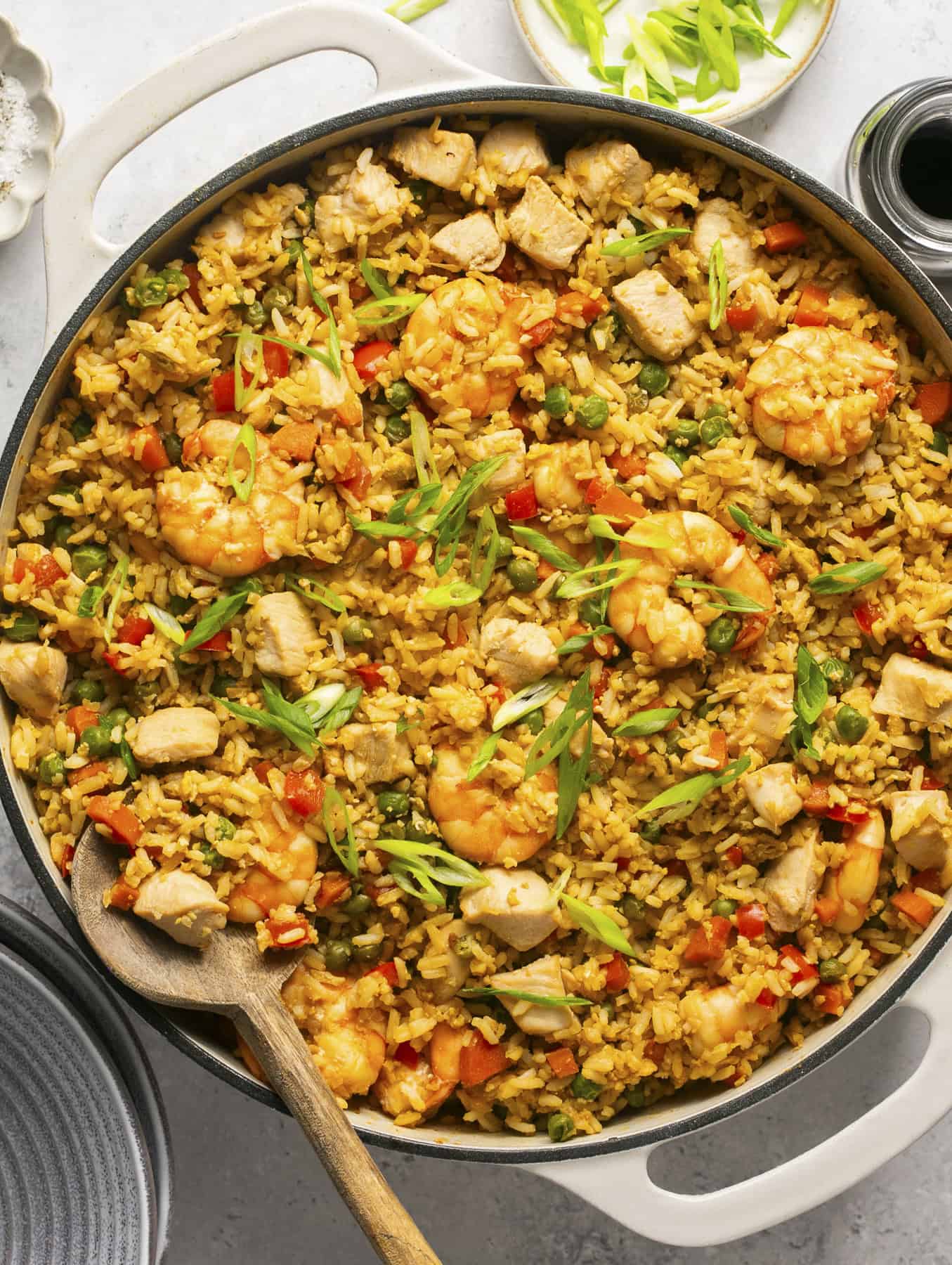 Chicken and shrimp stir fry in a pan with a wooden spoon and green onions on top.