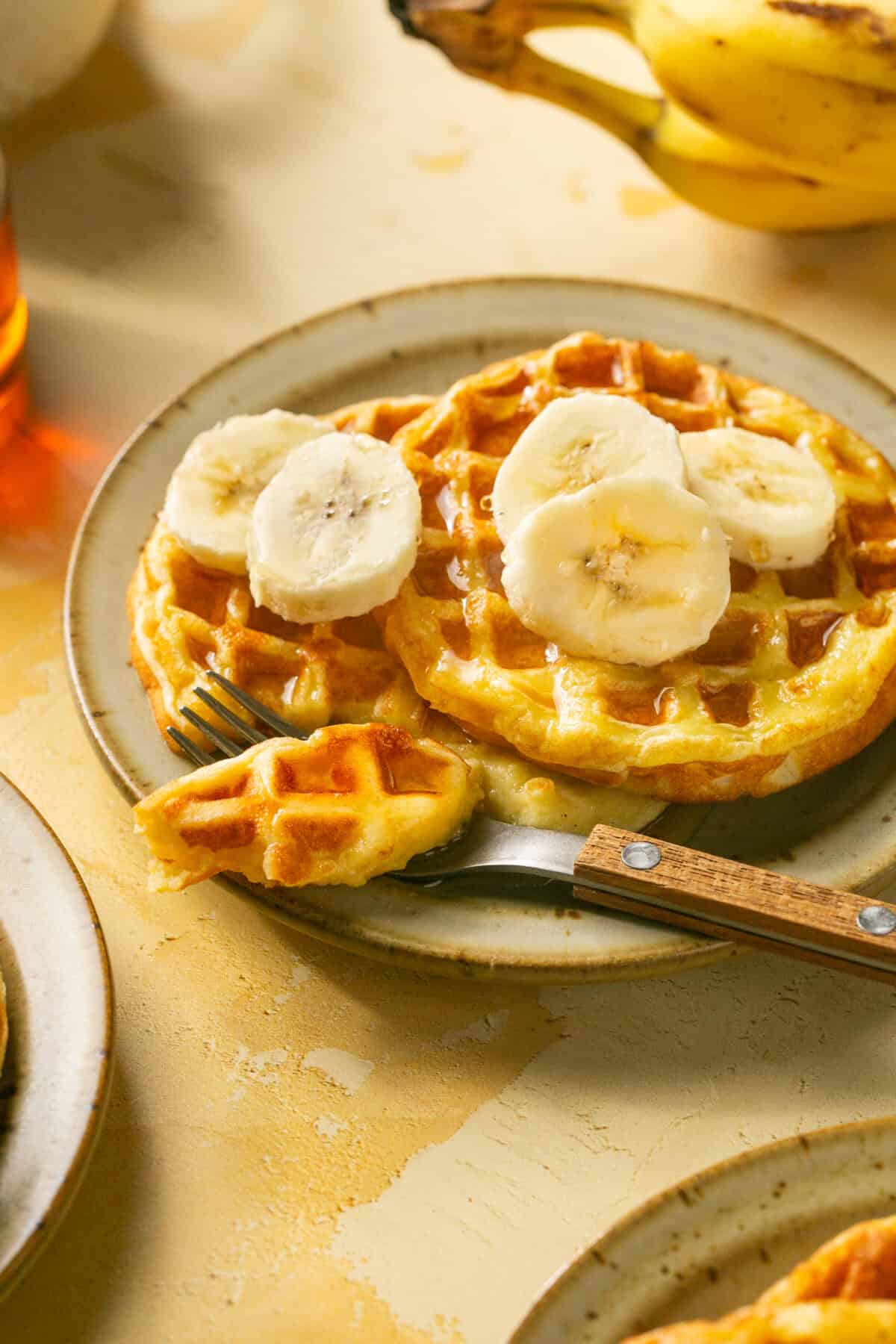 2 stacked waffles with banana and syrup on top and a piece cut out with a fork. 