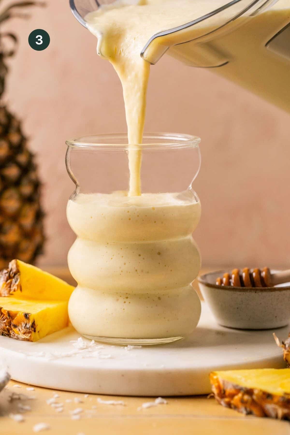 Tropical smoothie being poured into a cup from the blender cup with fresh cut pineapple around.