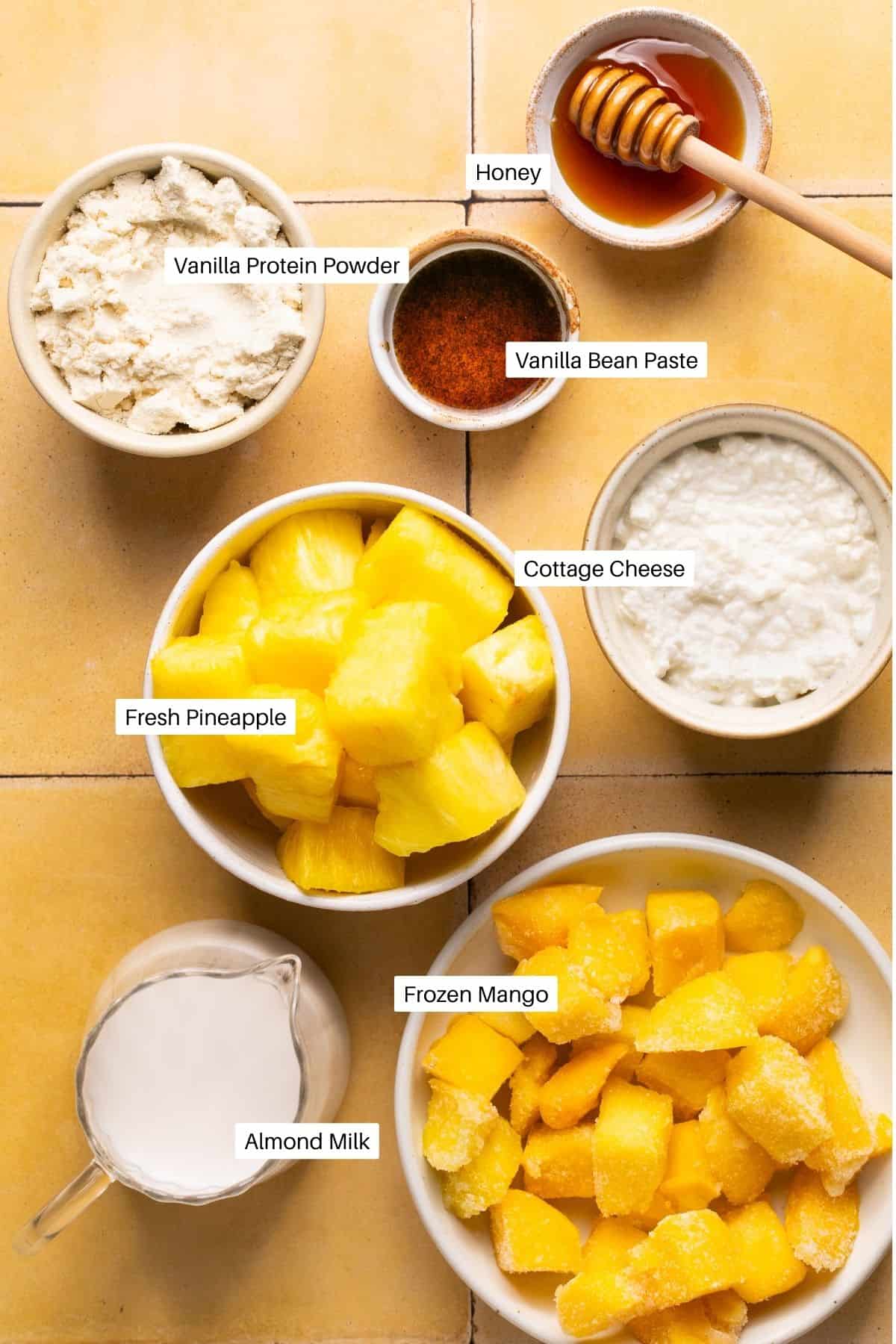 Protein powder, honey, vanilla bean paste, fresh pineapple. frozen mango, cottage cheese and almond milk for making a smoothie. 