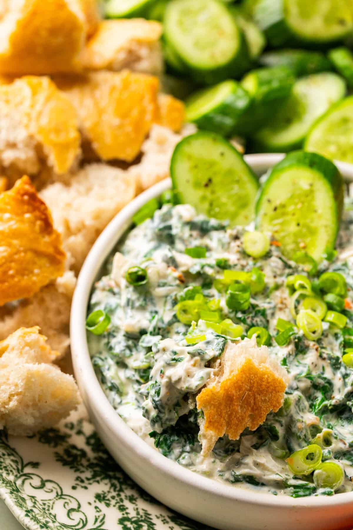 Spinach dip in a serving dish with green onions on top and bread dipped in. 