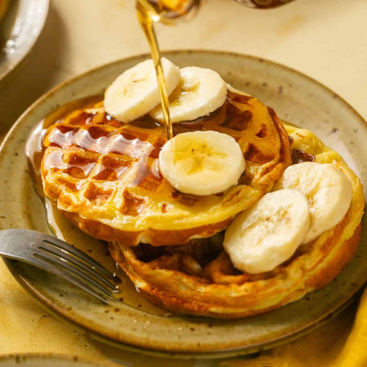 Two waffles with banana and syrup on top.