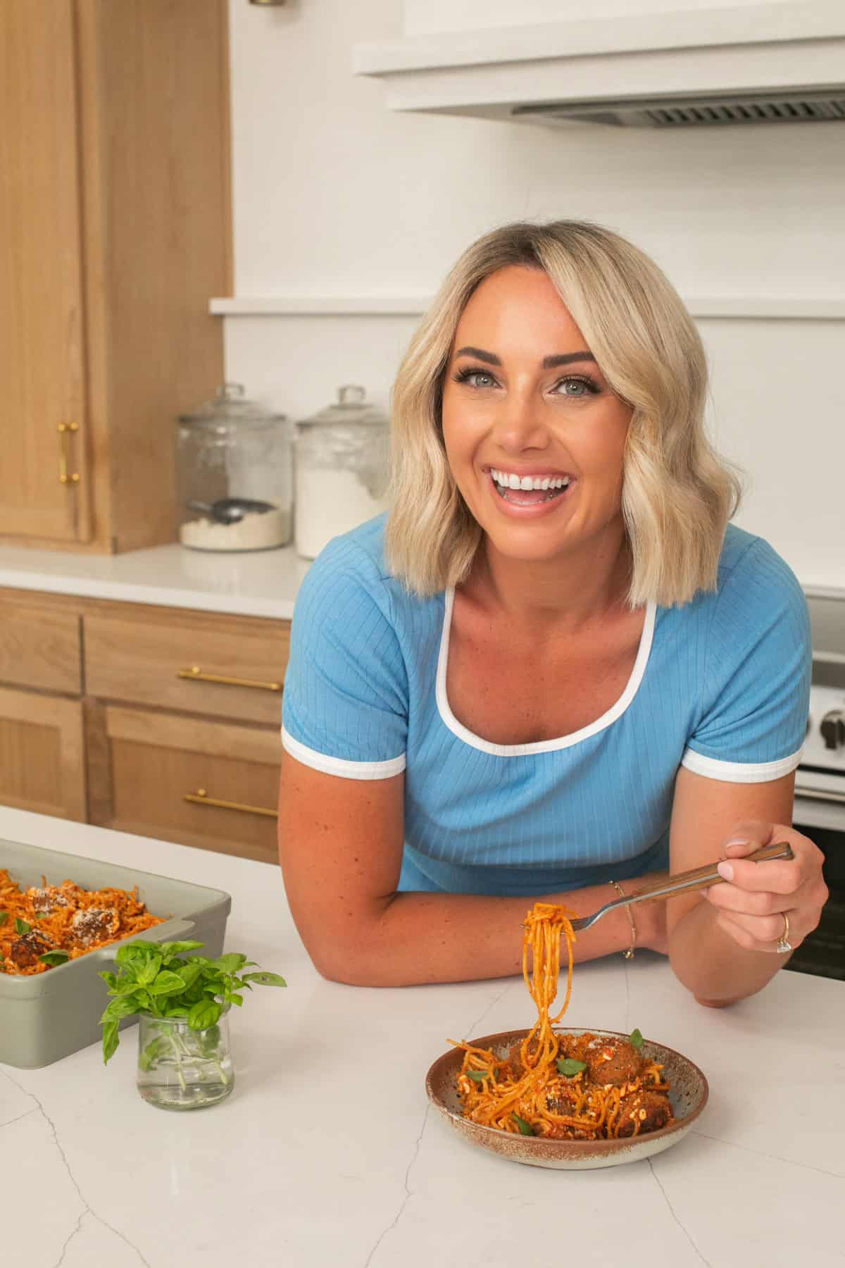 Danielle in a bright shirt in a kitchen with a plate of spaghetti and meatballs.