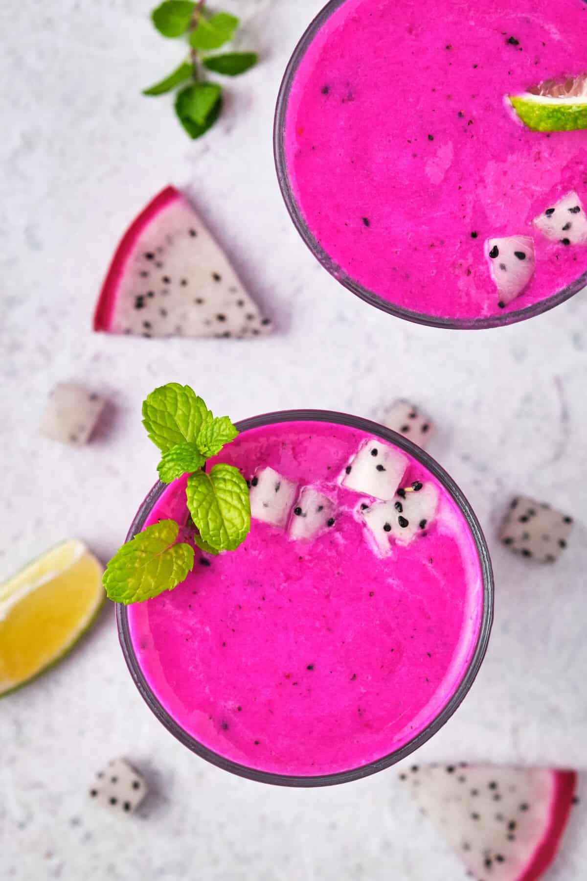 Overhead shot of two dragon fruit smoothies with fruit around. 