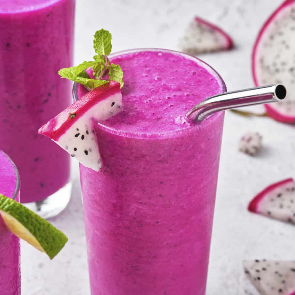 Vibrant dragon fruit smoothie with a piece of dragon fruit sliced on the top edge with a straw.