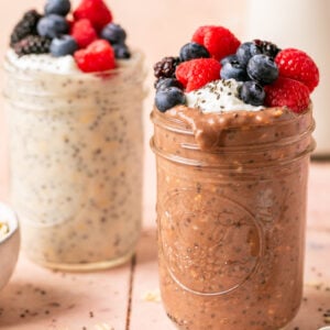 Two jars of overnight oats one chocolate and the other vanilla both topped with mixed berries, greek yogurt and sprinkle of chia seeds.