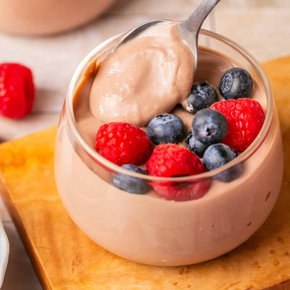 Pudding in a pudding cup with a spoon with some on it and berries on top.