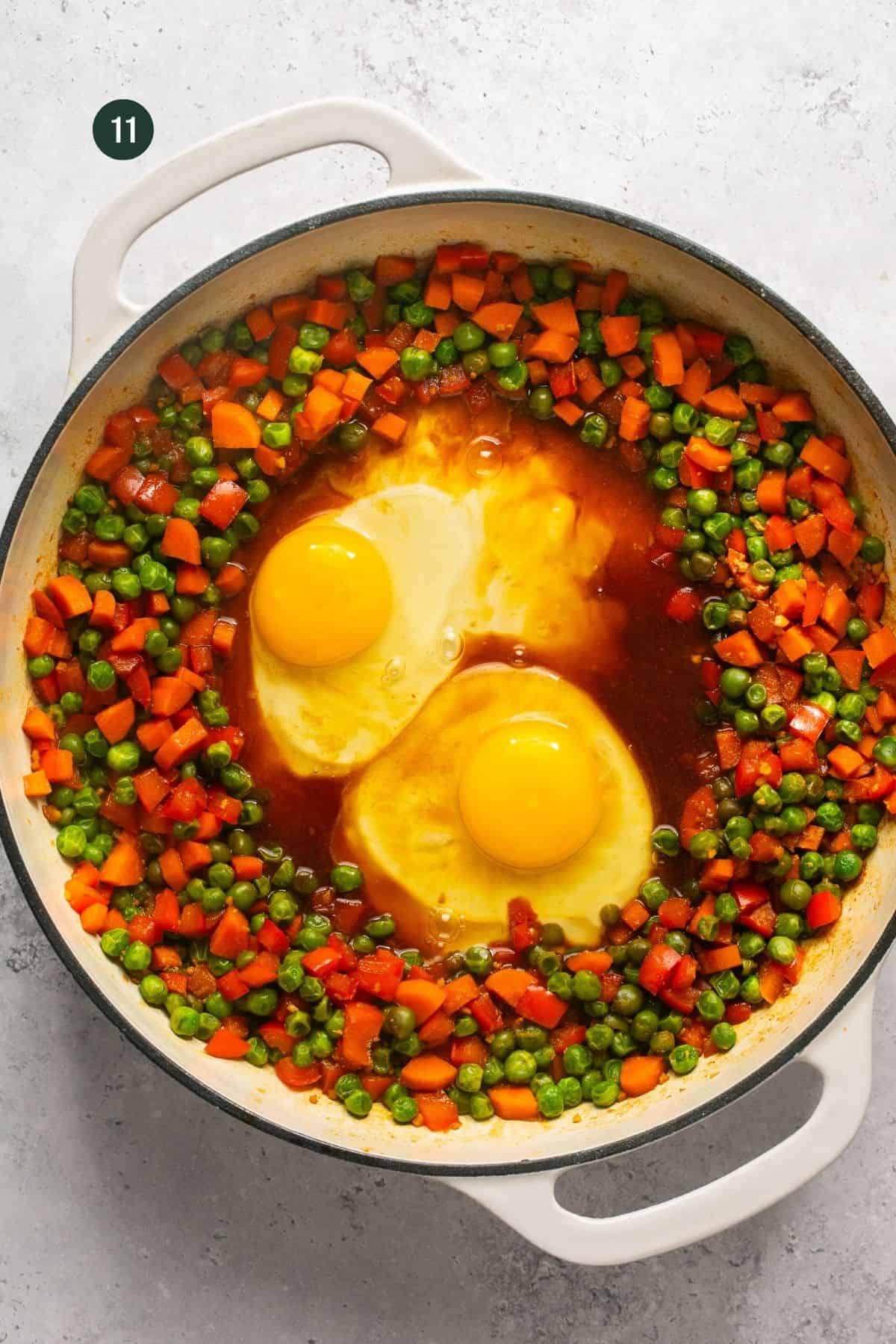 2 eggs cracked in the center of a pan with coconut amino sauce in the center and cooked veggies around the outside of the pan.