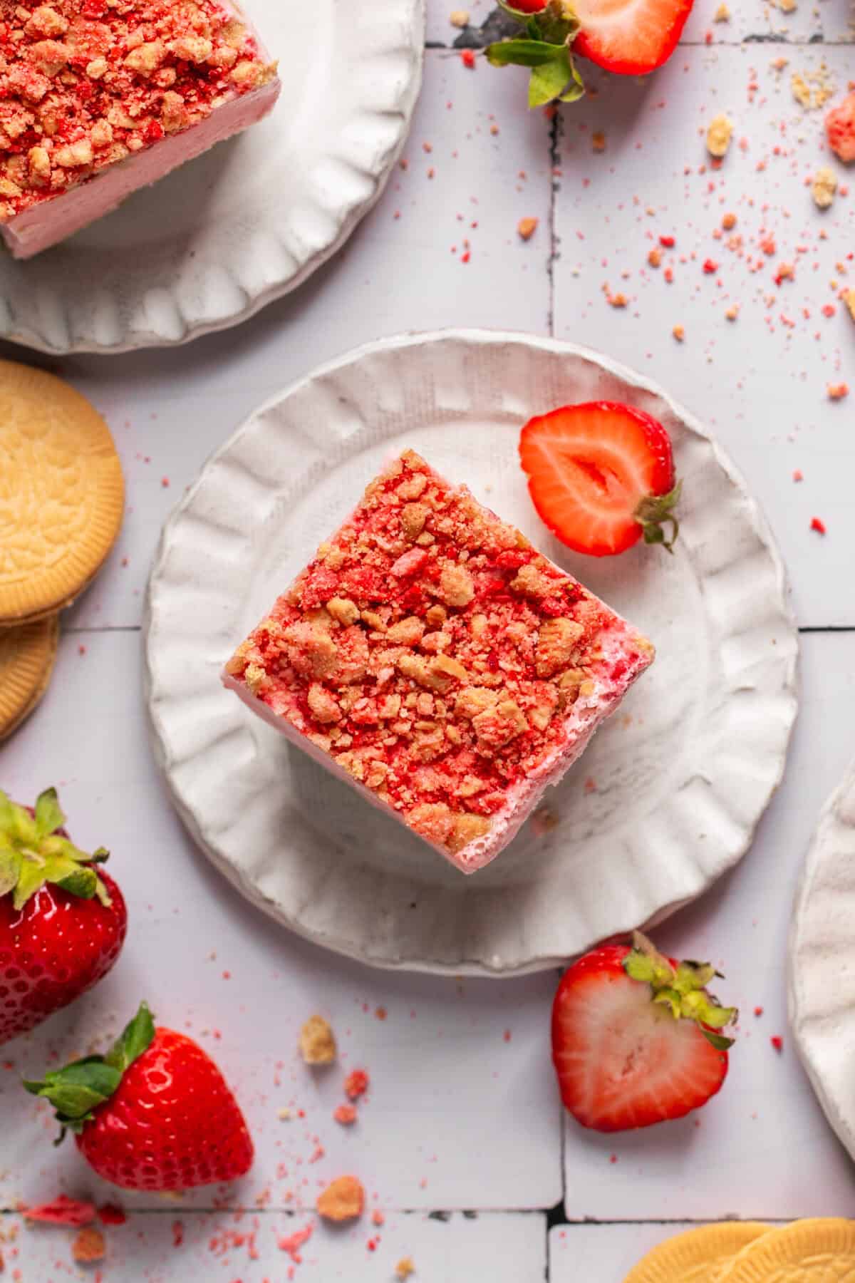 Overhead shot of one square of a strawberry crunch frozen ice cream bar on a plate with fresh strawberries around. 