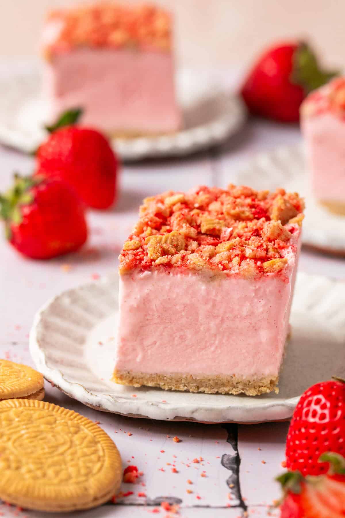 One ice cream square on a plate with other plated behind it and fresh strawberries. 