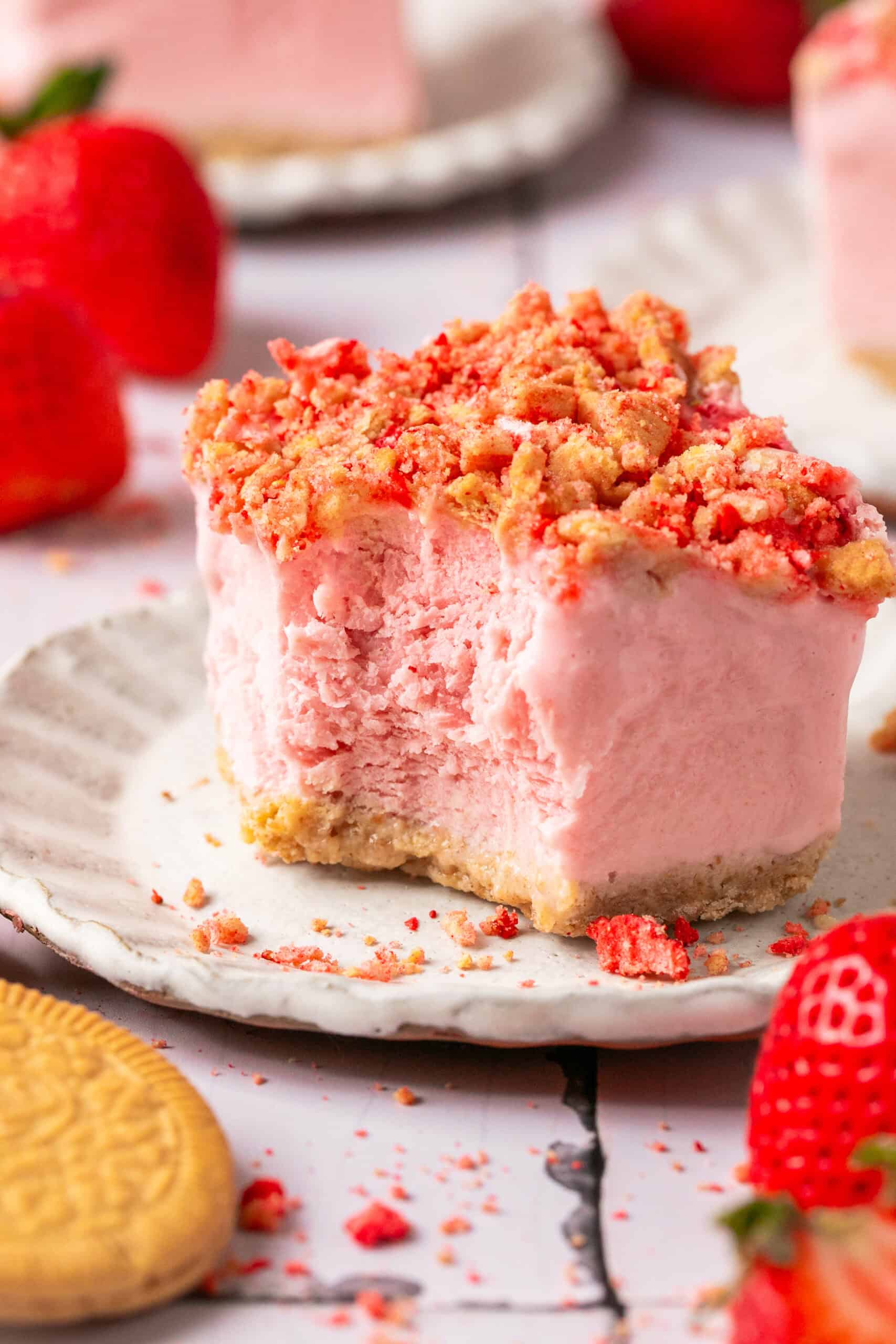 A bite taken out of one corner of a strawberry crunch frozen ice cream bar.