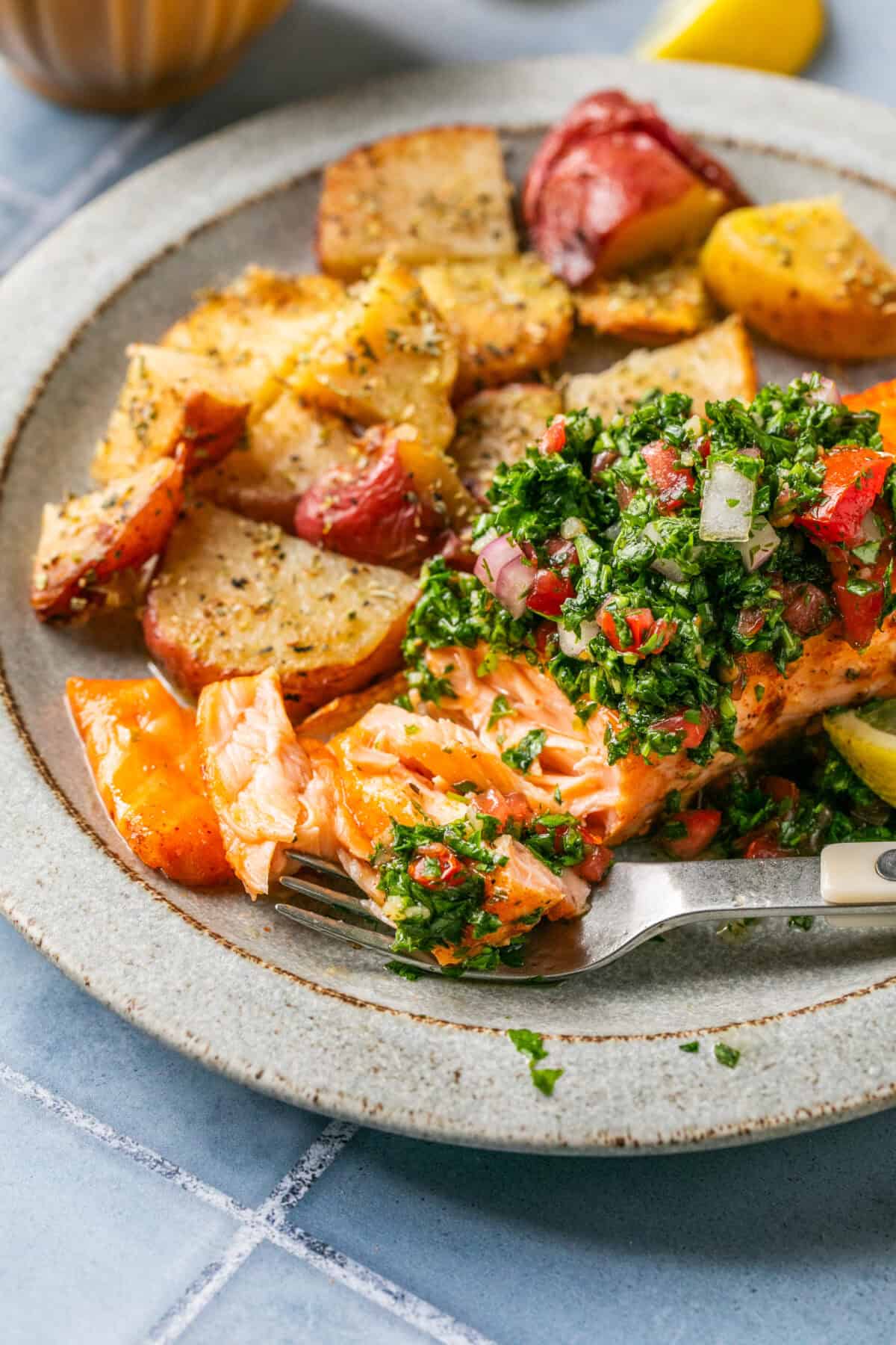 Flaked and cooked salmon with a fork topped with chimichurri sauce on a plate with roasted potatoes. 