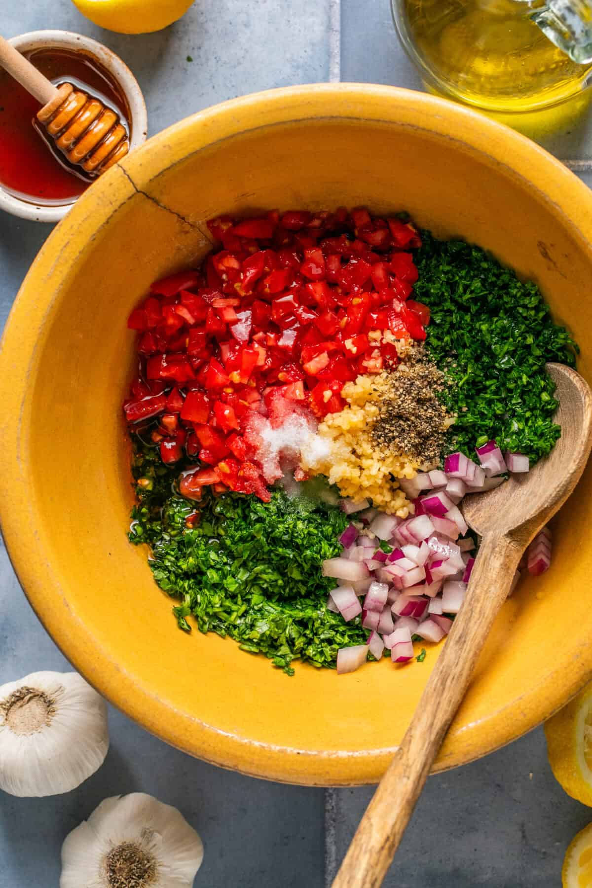 All chimichurri ingredients chopped and added to a large mixing bowl with a wooden spoon. 