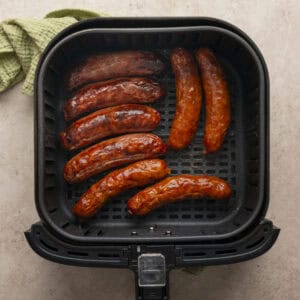 Air fried and browned chicken sausages in the base of a air fryer basket.