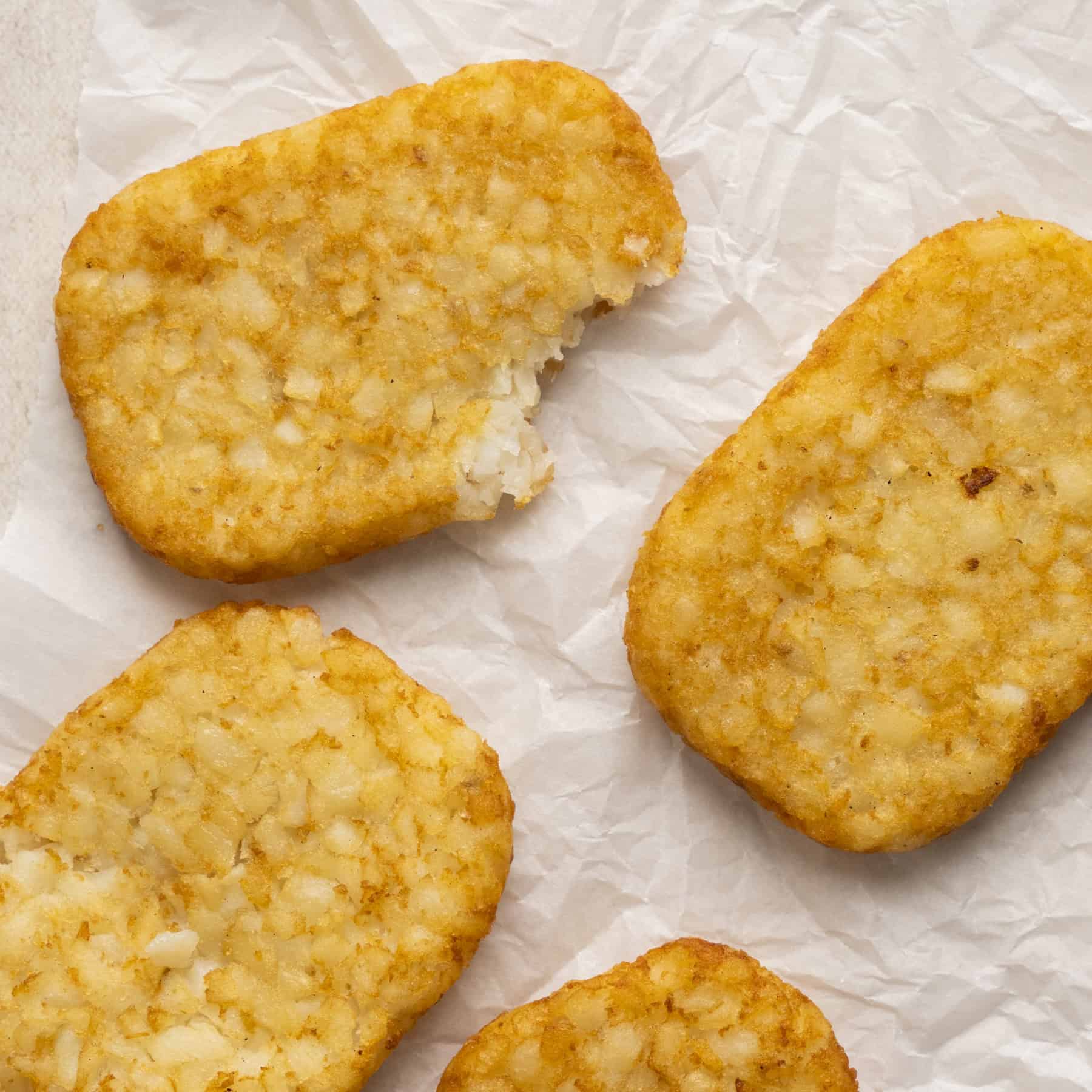 4 cooked hashbrowns laid out with a bite taken out of one.