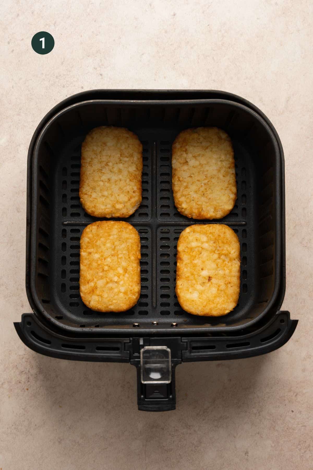 Cooked hash brown patties in the basket of a air fryer. 