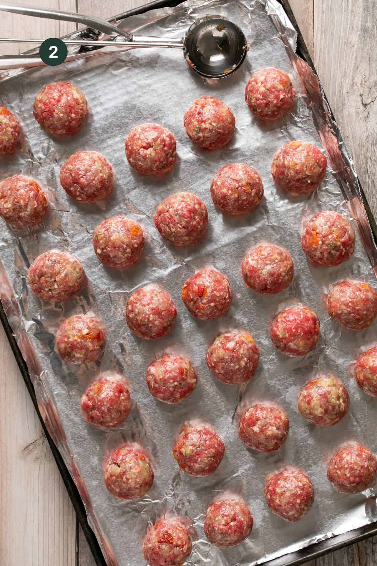 32 meatballs on a foil lined baking sheet with a cookie scoop used for forming the meatballs. 