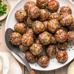 Plate full of cooked meatballs with parsley on top and a spoon for serving.