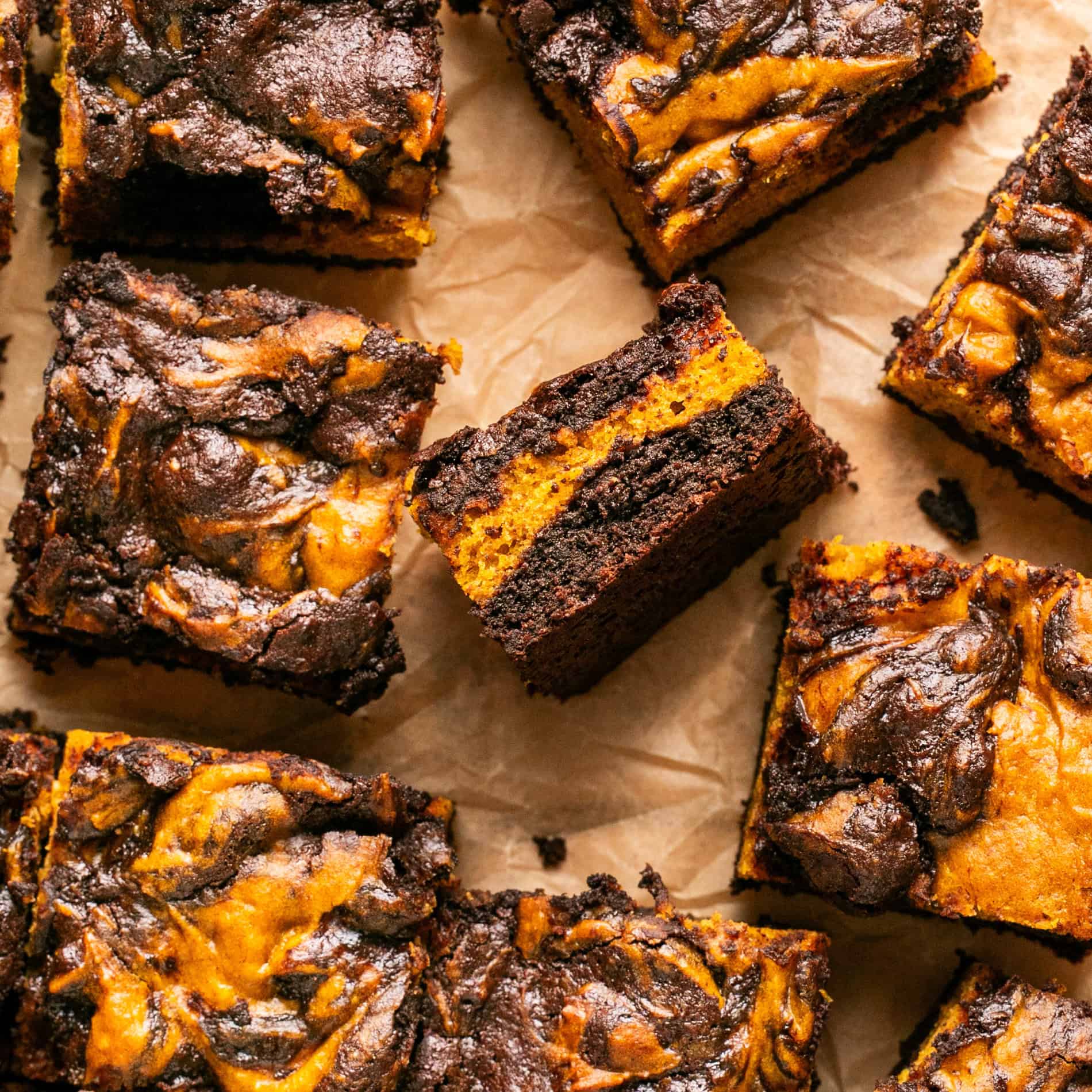 Chocolate and pumpkin swirled brownies laid out in squares with one to the side to show the inside layers.