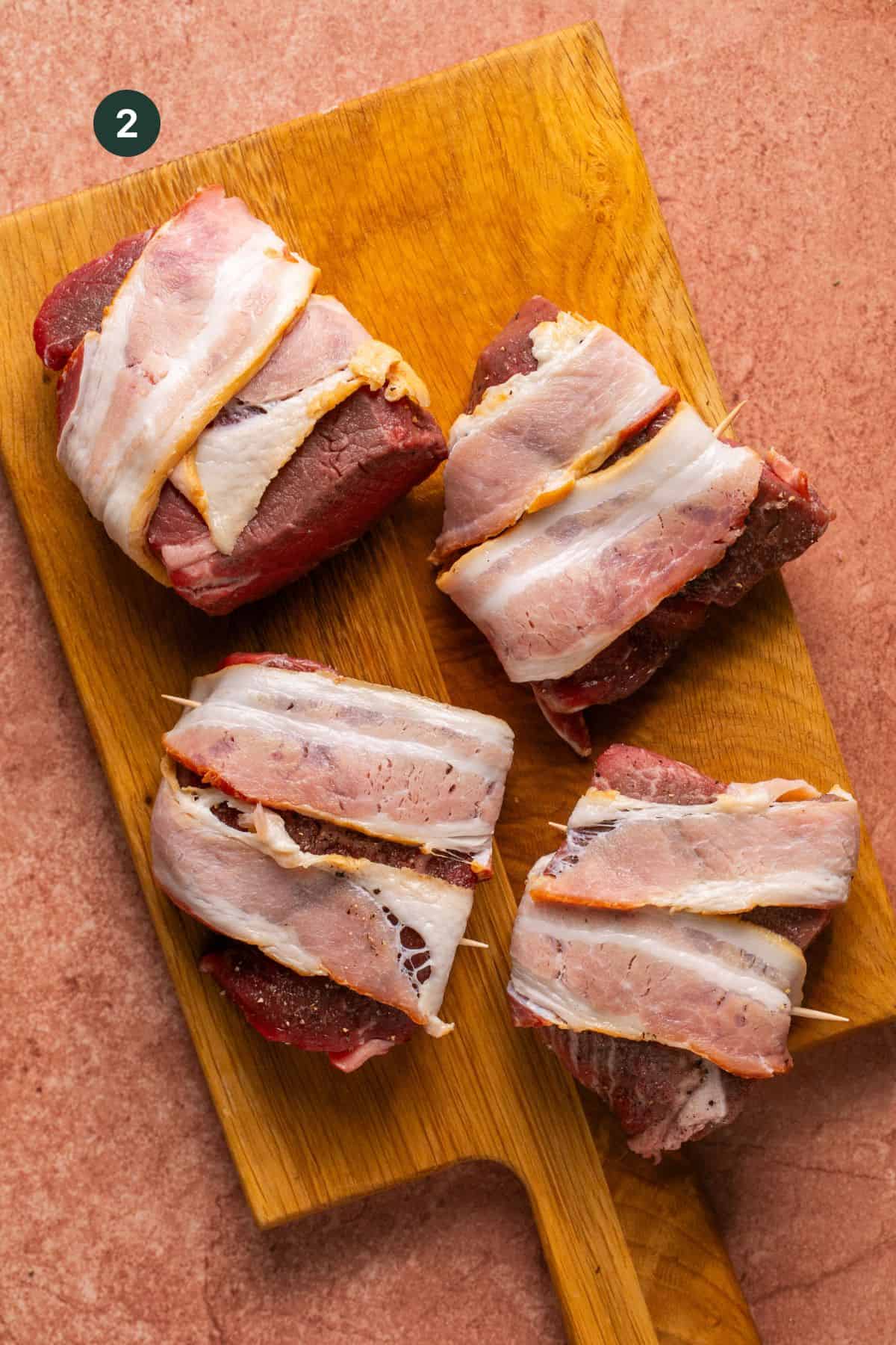 Filet mignon wrapped with bacon slices on a cutting board.