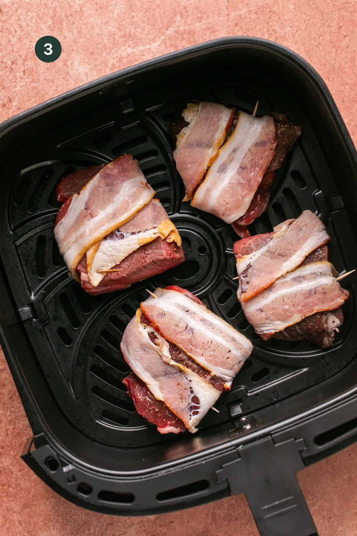 Bacon wrapped filets in the basket of the air fryer to cook.