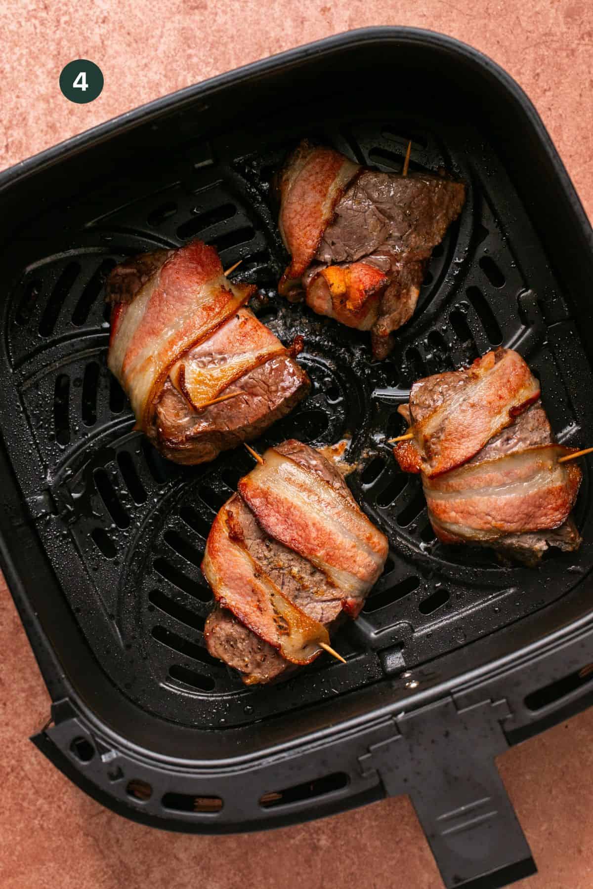 Cooked bacon wrapped filet mignon in the air fryer basket.