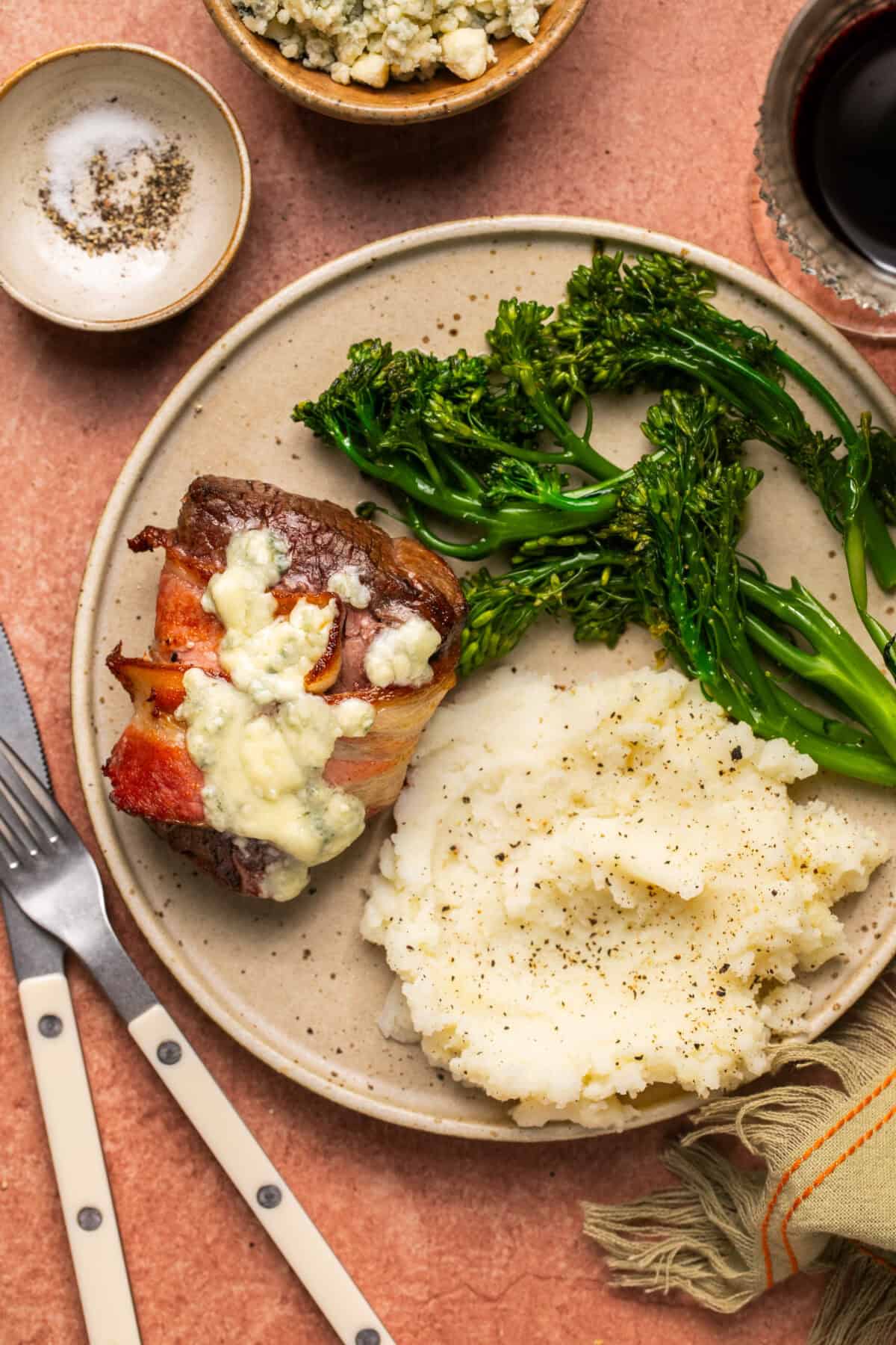 Plated filet with cheese on top and a side of mashed potatoes and broccolini. 