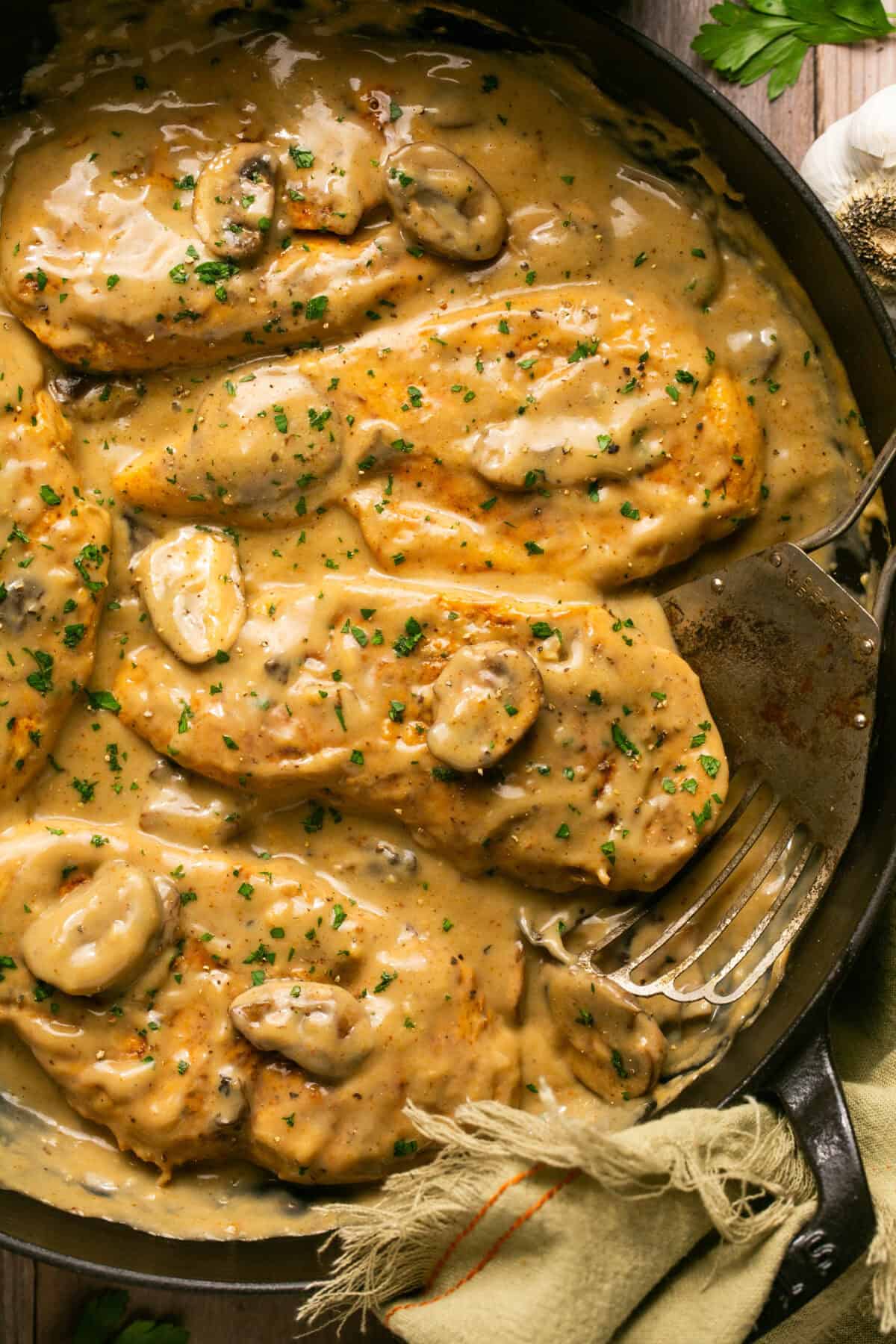 Creamy mushroom sauce chicken in a skillet with a spatula for serving.