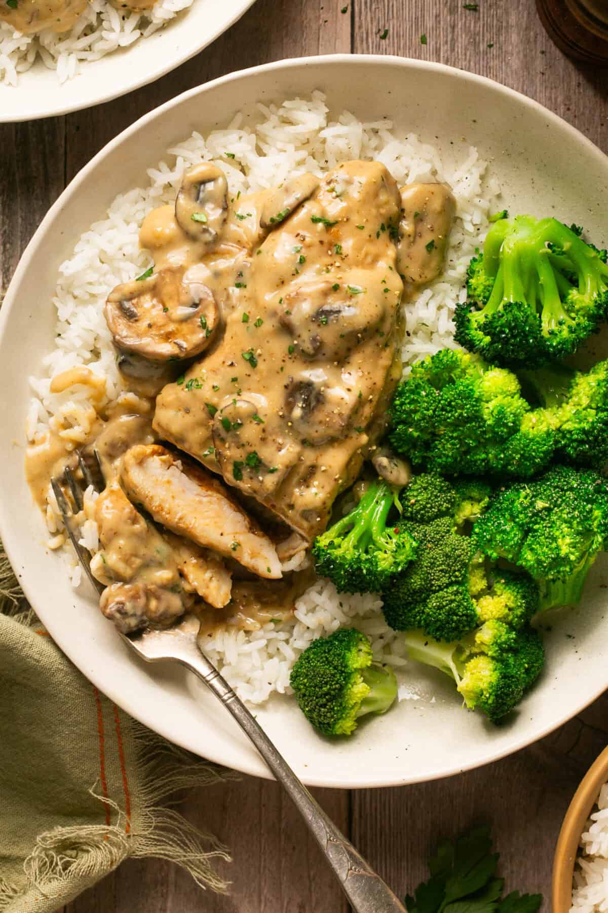 Creamy mushroom chicken over rice with a side of steamed broccoli on a plate with a fork. 