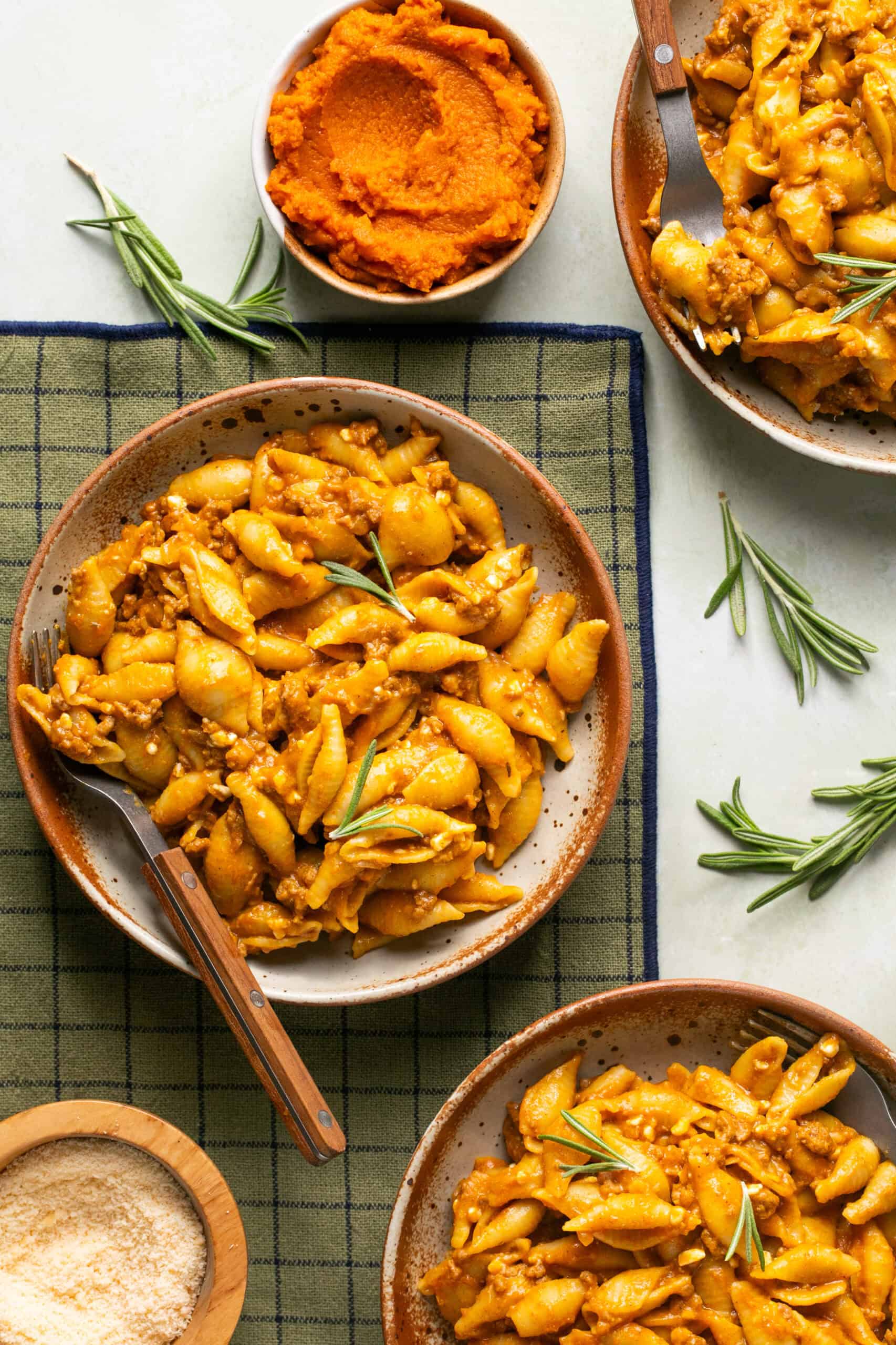 Pumpkin beef pasta plated on a placemat with a fork for eating with sprigs of fresh rosemary.