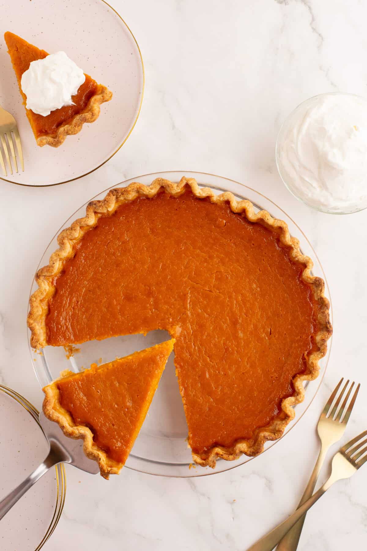 Baked sweet potato pie with a slice out with whipped cream on top on a plate and another being served. 